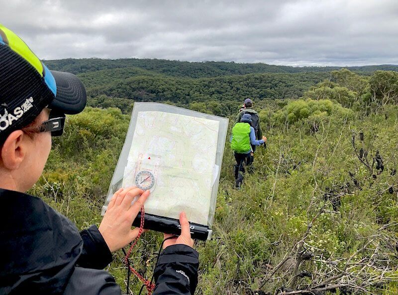 woman holds up topographic map and compass in bush