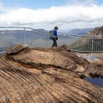 female hiker walks alongside cliff fence in blue mountains