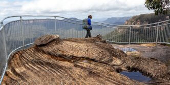 female hiker walks alongside cliff fence in blue mountains