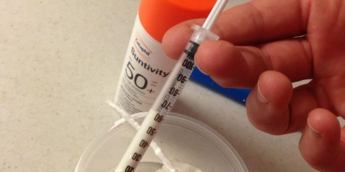 Using a syringe to transfer sunscreen to a tiny travel bottle.